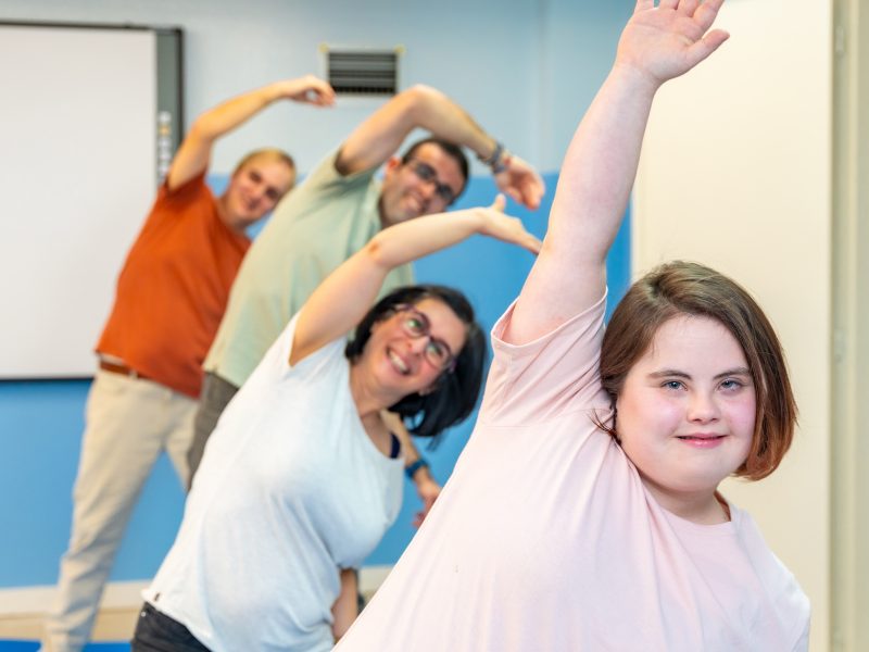 Focus on a woman with down syndrome and a group of people with special needs stretching in the gym